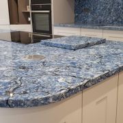 A shaker-style kitchen featuring a statement island, worktops, and full-height splashback in the dramatic, swirling blue and black ST Bayside stone