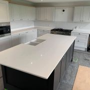 Large shaker-style kitchen featuring a dark grey island and light grey cabinets, all with a subtle and elegant white quartz worktop