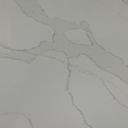 Close-up of an ST Quartz Calacatta Gold slab, featuring broad, grey marble-like veins with subtle, warm gold highlights on a soft white background