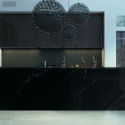 A luxury black kitchen featuring a monolithic island with Nile Quartz Marquina Shimmer waterfall worktops