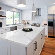 A beautiful all-white kitchen design showcasing the bold, grey veining of Nile Quartz Calacatta on a large central island